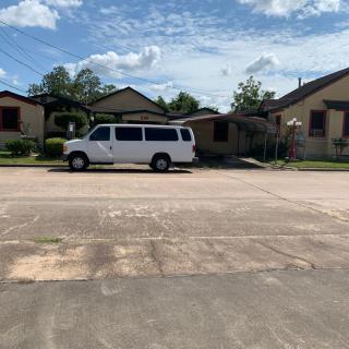 A white van parked on a street in a residential neighborhood under a sunny sky with scattered clouds.