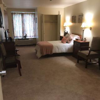 A cozy bedroom with a neatly made bed, chairs, bedside lamps, and a large window.