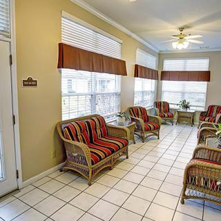 A bright waiting room featuring wicker furniture with striped cushions and large windows allowing natural light.