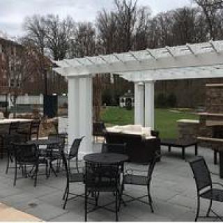 A patio area featuring a white pergola and outdoor furniture set in a landscaped environment.