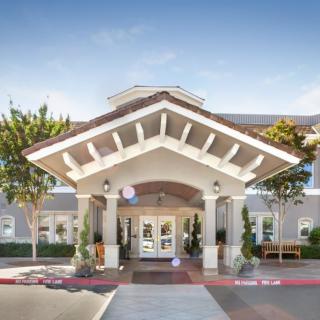 The front entrance of a modern building with an overhang and landscaped surroundings.