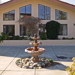 A three-tiered fountain stands in front of a building with large windows and a well-maintained garden.