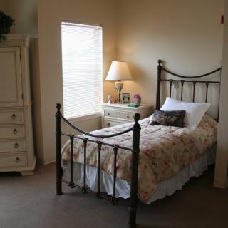 A cozy bedroom with a single metal-framed bed, bedside lamp, and dresser.