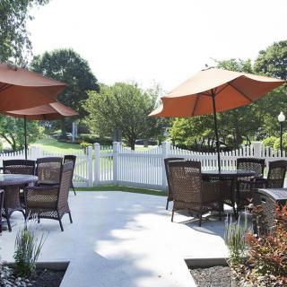 A peaceful outdoor patio area with tables, chairs, and umbrellas set against a garden backdrop.