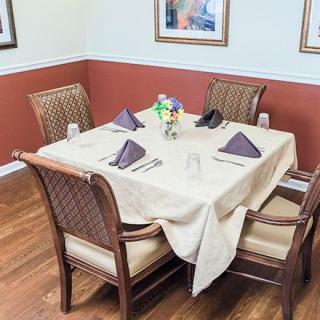 A neatly set dining table with four chairs, adorned with napkins and a flower centerpiece in a cozy restaurant setting.