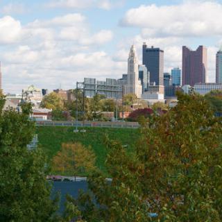A scenic view of a city skyline framed by greenery and clouds, showcasing a blend of nature and urban architecture.
