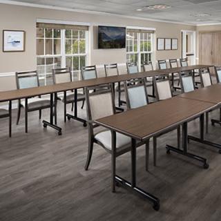 A modern conference room setup with long tables and chairs, featuring a television and large windows.