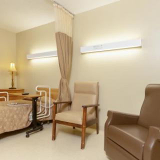 A well-furnished hospital room with a patient bed, comfortable chairs, and soft lighting.