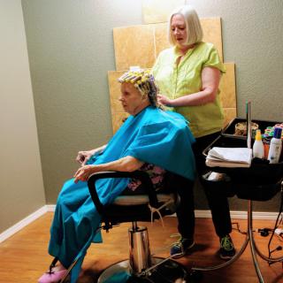 A hairdresser styles a senior's hair in a salon setting.