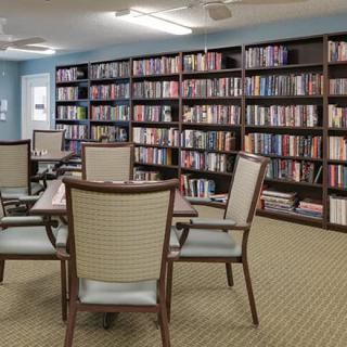 A quiet library room with bookshelves filled with books and a table with chairs arranged for reading or study.