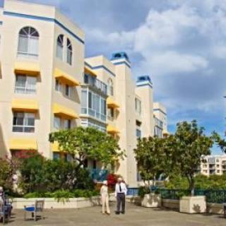 A residential apartment building with people walking and greenery around.