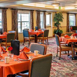 A well-decorated dining area with neatly arranged tables and chairs, featuring orange tablecloths and floral centerpieces.
