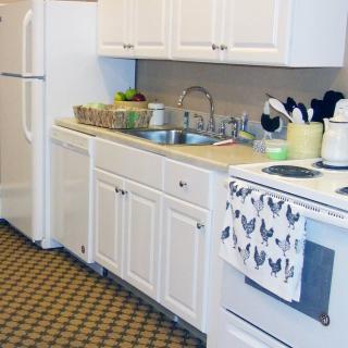 A clean and organized kitchen with white cabinets, a refrigerator, oven, and sink.