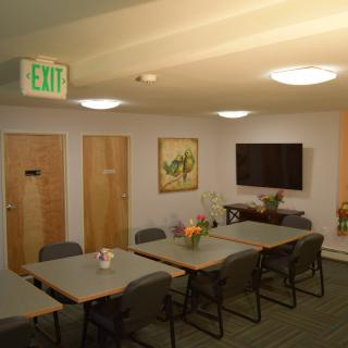 A well-lit conference room with tables, chairs, a television, and artwork on the walls.