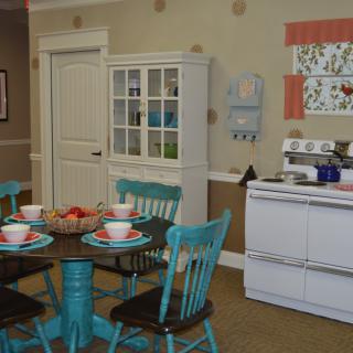 A cozy vintage kitchen and dining area with turquoise chairs, a dark wooden table set for a meal, and a white stove.