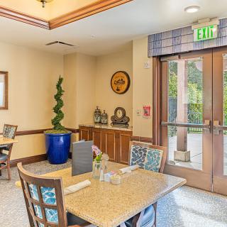 A cozy dining area with a table set, decorative plants, and natural light streaming through the glass door.