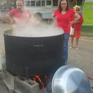 People cooking in a large pot outdoors at a festival.