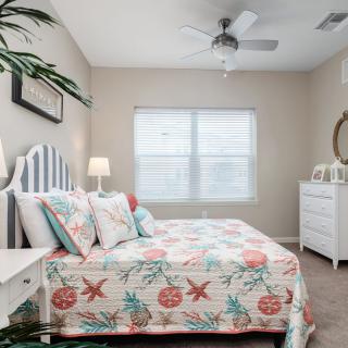A cozy bedroom with a colorful quilt and matching pillows on the bed, a ceiling fan, and a dresser near the window.