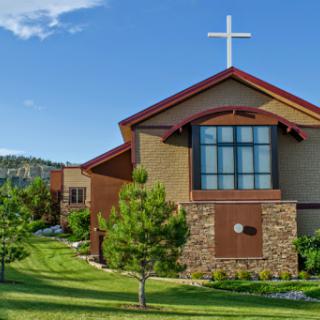 A beautiful church featuring a prominent cross, surrounded by lush greenery and under a clear blue sky.