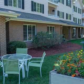 A patio set in a garden area outside of a residential building, surrounded by greenery and flowers.