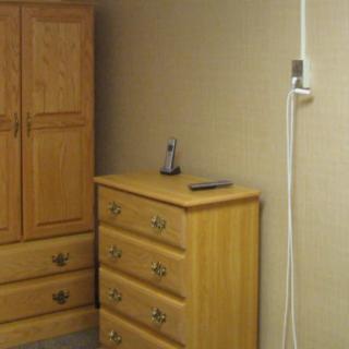 A wooden dresser and wardrobe in a room, with a small ornament and a phone on top of the dresser.