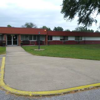 A view of a single-story educational building with a red roof and surrounding green space.