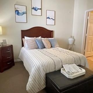 A cozy bedroom with a neatly made bed, decorated with pillows and artwork on the walls.