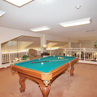 A spacious game room featuring a pool table with cues and balls on it, surrounded by seating and recreational space.