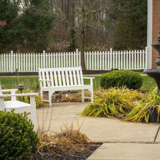 A serene garden patio with white benches and lush greenery.