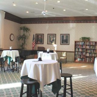 A cozy dining area with round tables and a library shelf, decorated with framed pictures and an American flag.