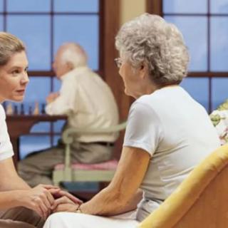 A caregiver engaging in conversation with an elderly person in a nursing home setting.