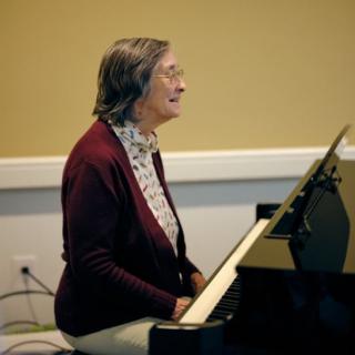 An elderly woman playing the piano indoors.