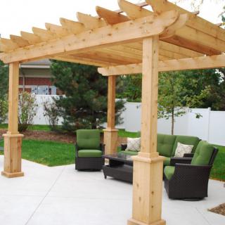 A wooden pergola with outdoor seating in a backyard setting.