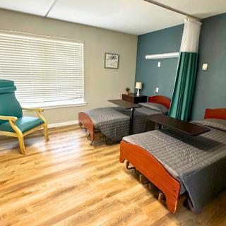A spacious hospital room featuring two beds, wooden flooring, and a cozy seating area by the window.