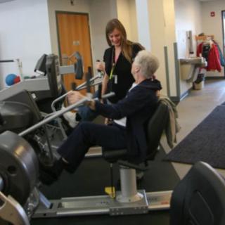 A senior person working out at the gym with assistance from a trainer.