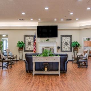 A cozy living room setting with a central seating arrangement, wall-mounted television, and fireplace surrounded by decorative plants.