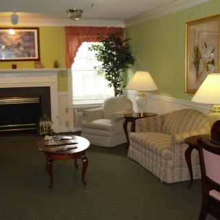 A cozy traditional living room with a sofa, armchairs, a coffee table, and a fireplace, adorned with artwork and an indoor plant.