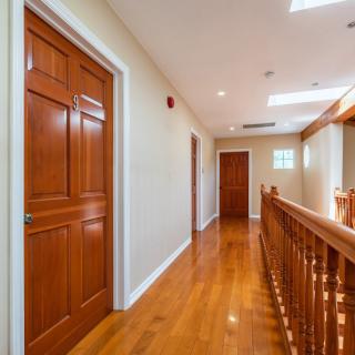 A hallway with polished wooden floors and doors, featuring a banister and recessed lighting.