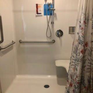 An accessible shower equipped with a grab bar, shower seat, and floral curtain.