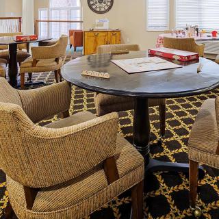 A cozy lounge area with a round table surrounded by upholstered chairs, a patterned carpet, and board games on the table.