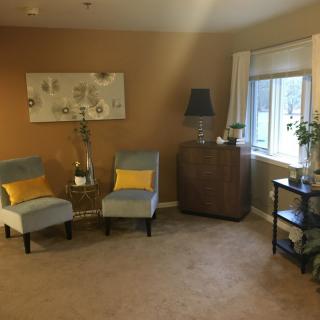 A cozy living room with neutral tones and yellow accents, featuring two chairs, a side table, and a window bringing in natural light.