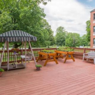 A spacious outdoor deck with a swing, picnic tables, and benches surrounded by lush greenery.