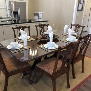 A dining area featuring a glass-top table set for six with elegant place settings and wooden chairs.