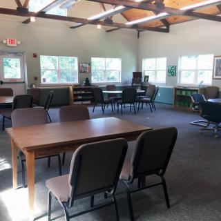 A bright and spacious meeting room with tables, chairs, and large windows letting in natural light.
