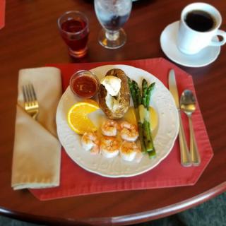 A breakfast plate featuring shrimp, asparagus, orange slices, and a potato dish, accompanied by a cup of coffee and juice.
