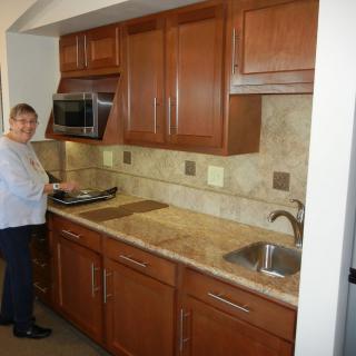 A woman standing in a kitchen with wooden cabinets and a granite countertop.