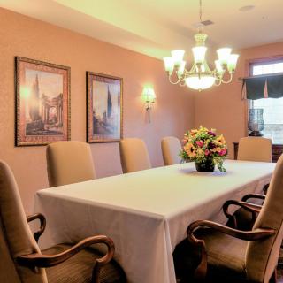A dining room featuring a long table with a white tablecloth, flanked by upholstered chairs, under an elegant chandelier.