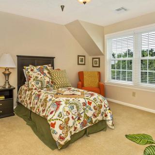 A cozy bedroom with a single bed, colorful bedding, and a large window.