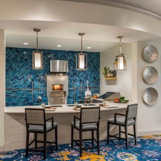A modern kitchen with a blue mosaic backsplash, pendant lights, and bar seating.