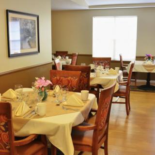 A well-arranged dining area with elegantly set tables and chairs, adorned with flowers.